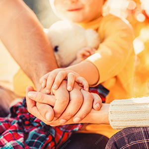 Ein Kind mit seinen Eltern, welche ihre Hände aufeinander gelegt haben